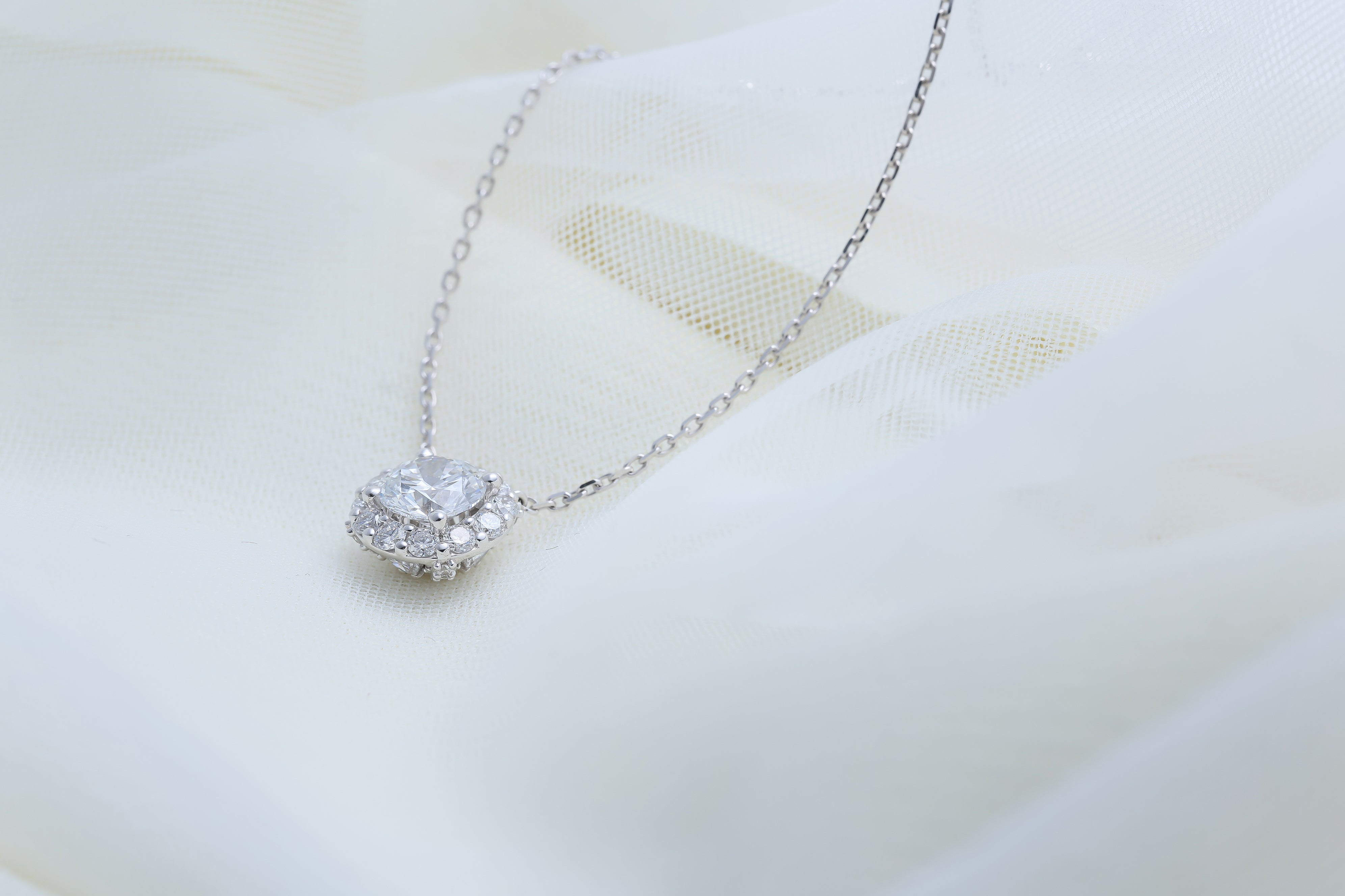 Fleur de Promesse ネックレス。チュール生地の上に置かれ、センターダイヤと取り巻きダイヤの輝きが際立つ上品なイメージショット。